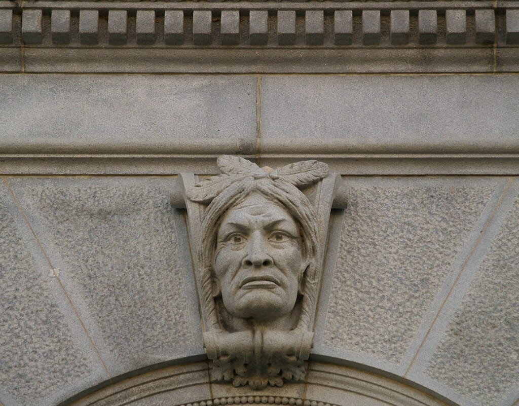 An Indian head carved on keystone - sits on top of arch made of stone.