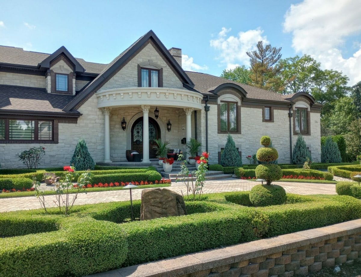 This beautiful home in Dearborn, Michigan has an interesting roof line, stunning front doors, classical pillars, and sculptured landscape. Photo by Doug Vos.