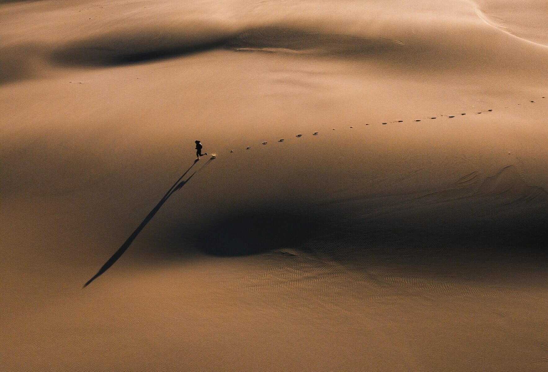 A long shadow appears as a man runs across the sands of time. A large sand dune in Bobs Farm NSW 2316, Australia.