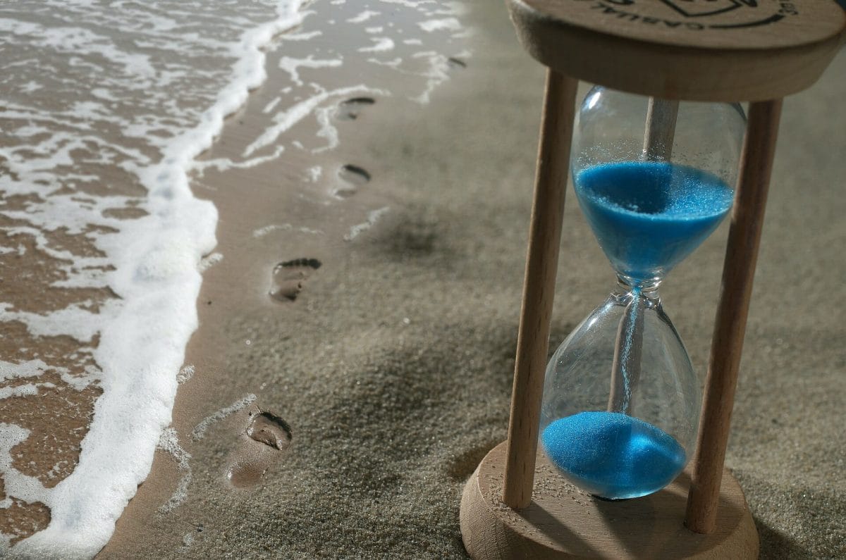 Footprints in the sand, on the beach, near an hourglass, depicting the sinking, shifting, sands of time.