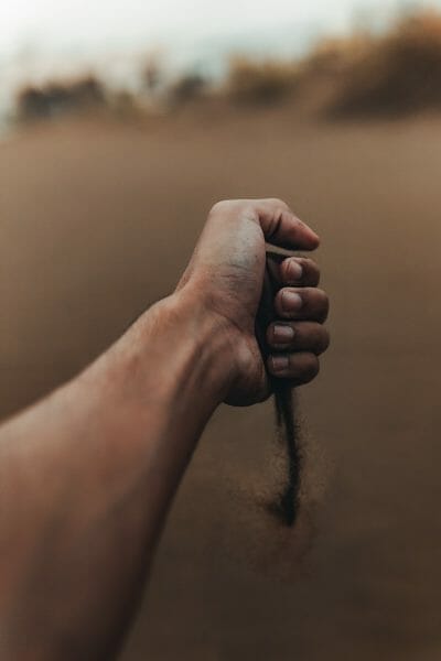 A hand grasping sand, with the sand slipping away.