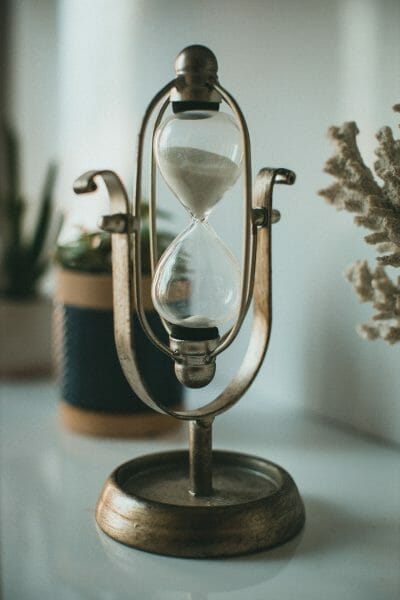 An old, brass hourglass. The frame appears to be made of brass, and the hourglass is filled with white sand. Sands of time photography.